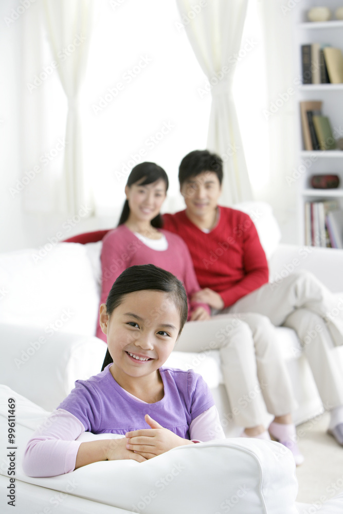 Young Chinese girl in a living room with parents in the background Young Chinese girl in a living room with parents in the background