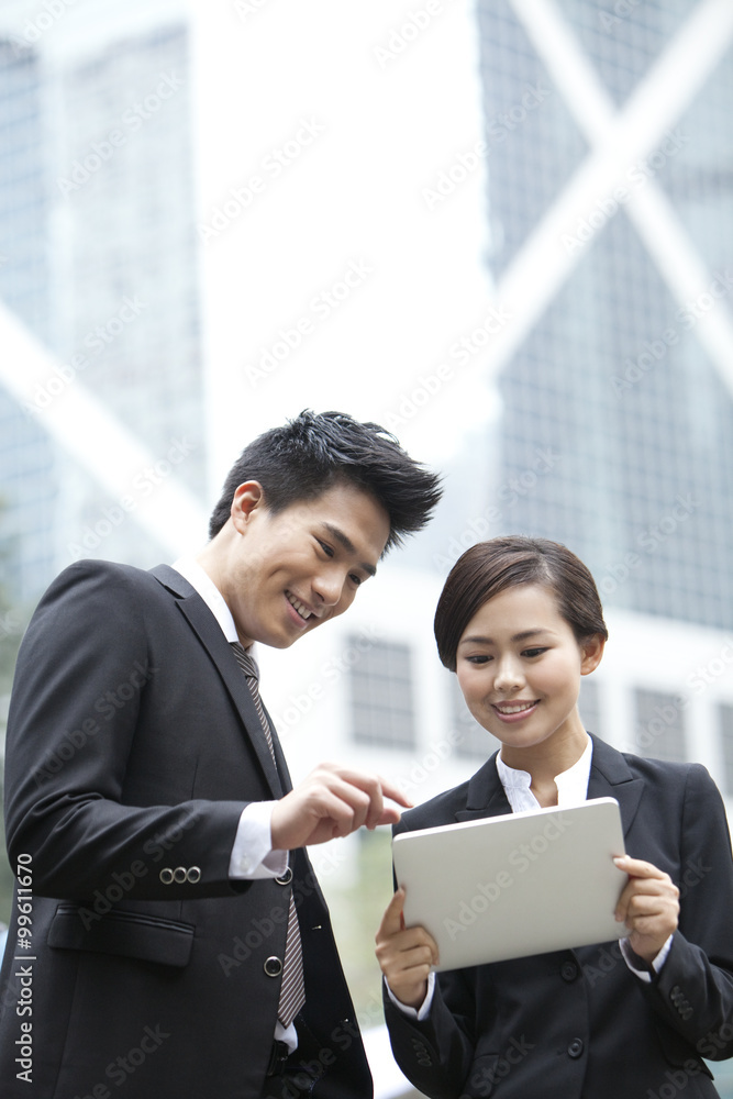Happy business colleagues using digital tablet together outdoors, Hong Kong Happy business colleagues using digital tablet together outdoors, Hong Kong