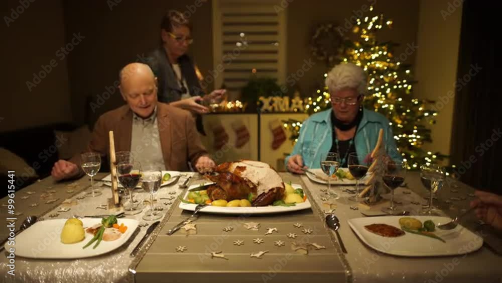 4k footage, seniors sitting on dining table at home on christmas eve with roasted turkey and woman putting jus  on plates, captured with atomos shogun
