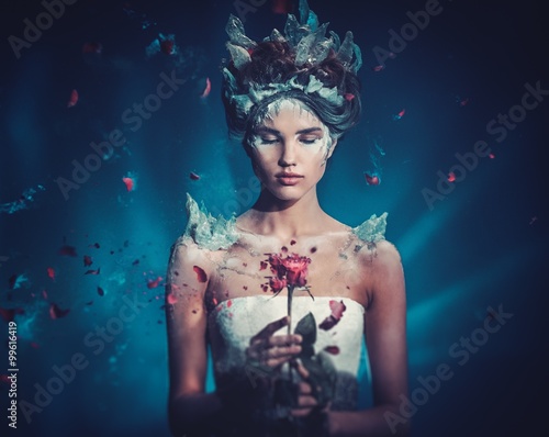 Winter beauty fantasy woman portrait. Beautiful young model girl and blast of frozen rose.