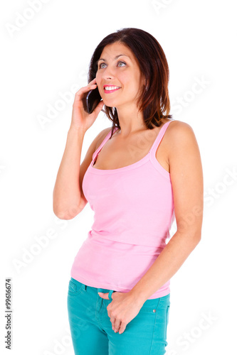 Portrait of smile slim brunette tanned woman with short hairstyle, dressed in t-shirt pink color and turquoise jeans, talking by cell mobile phone. Isolated on white background. Positive emotion