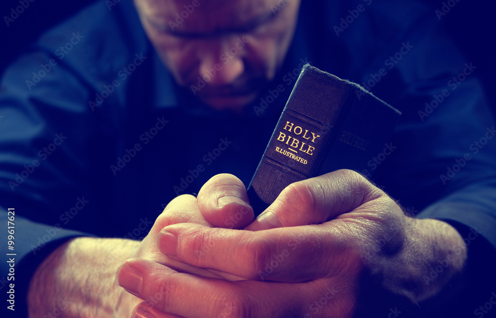 A Man praying holding a Holy Bible.