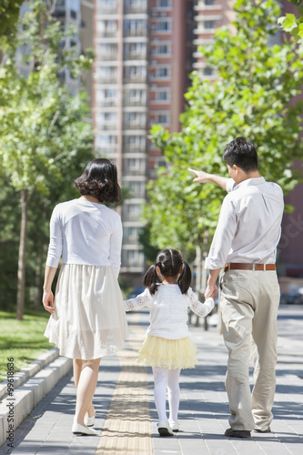 Young parents with daughter strolling on sidewalk hand in hand
