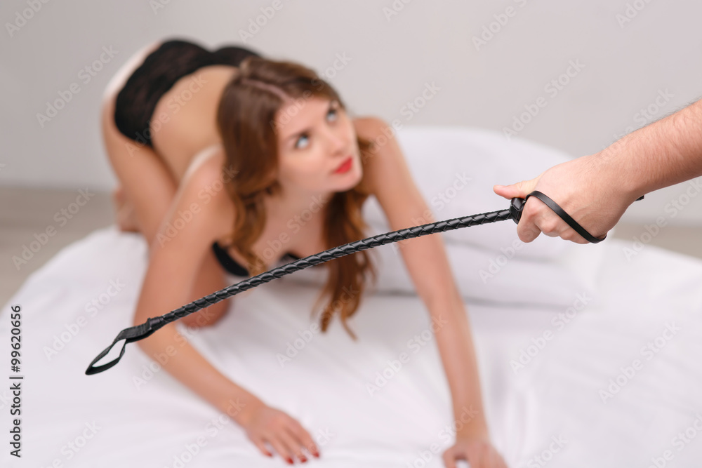 Sexual woman on bed and man holding a whip. Stock Photo