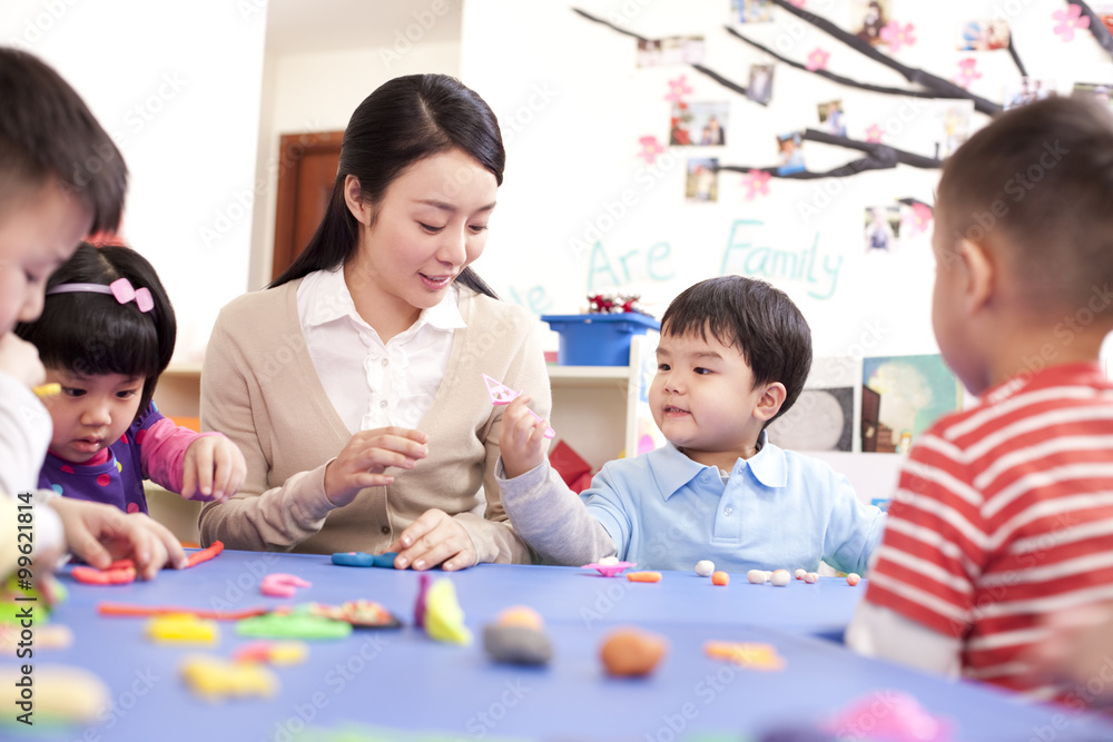 Kindergarten teacher and children playing with plasticine