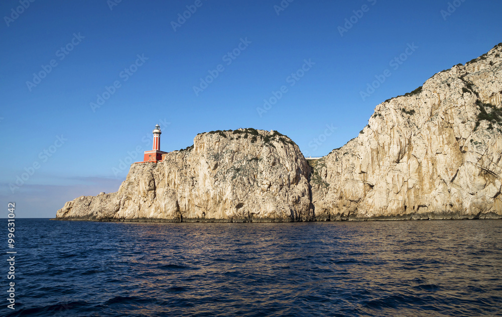 Punta Carena Lighthouse on the coastal rocks at the Mediterranean Sea in Capri island, seen from a motor boat tour.