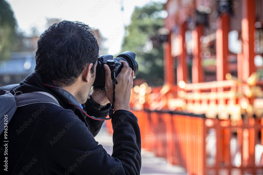 Obraz premium a man holding his camera taking photo of red Japanese temple or Fushimi Inari Shrine