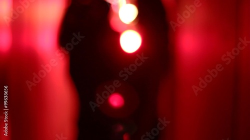 Silhouette of two sexy women dancing in a blurry, red corridor with her hands raised. Medium shot.
