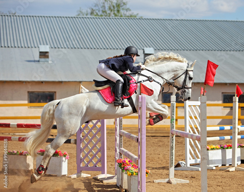 Teenage girl rider going over oxer spread jump on white horse