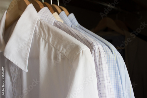 Several male shirts in light colors on wooden hangers in wardrobe
