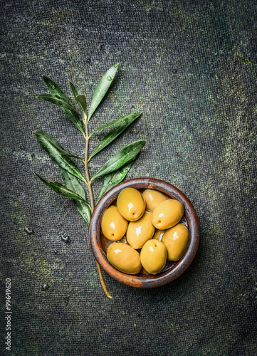 Olives in rustic bowl with oil and olive branch on dark vintage background  top view