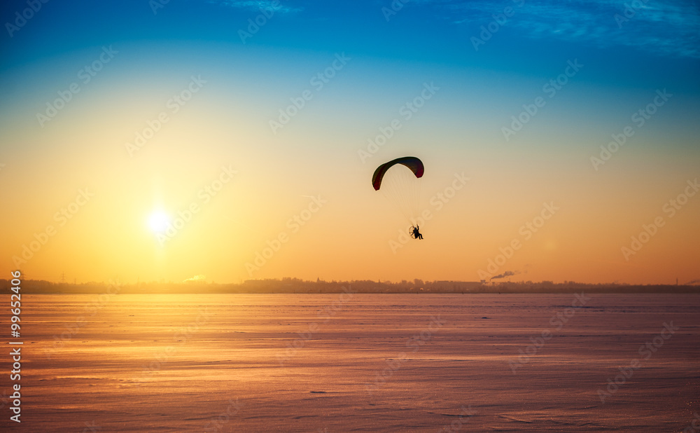 Beautiful winter sunset landscape with flying paraglider
