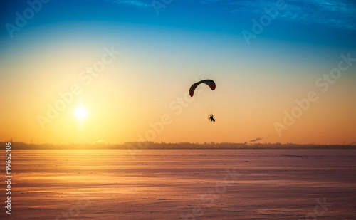 Beautiful winter sunset landscape with flying paraglider