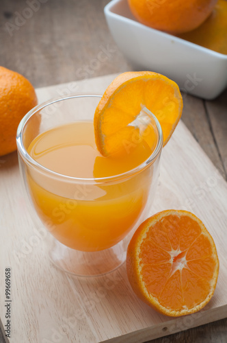 Orange juice glass on a wooden cutting board and wooden floors.