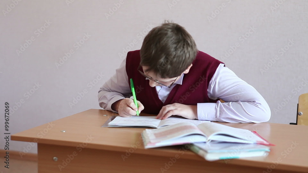 boy with glasses writes in a notebook sitting at a desk boy with glasses writes in a notebook sitting at a desk