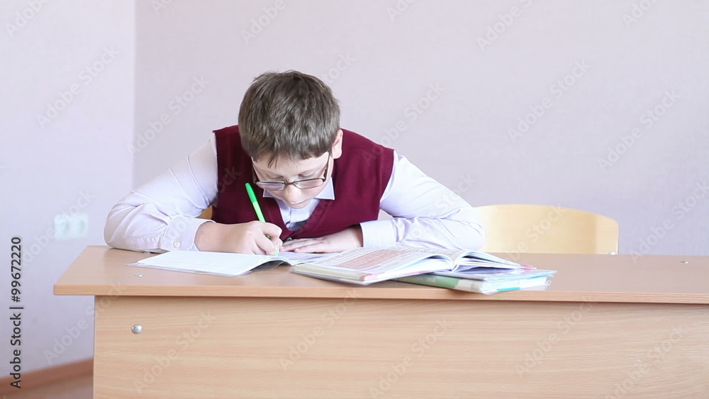 boy with glasses writes in a notebook sitting at a desk boy with glasses writes in a notebook sitting at a desk