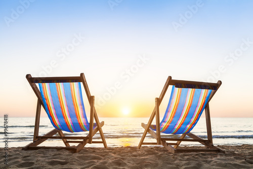 Two deck chairs on a sandy beach at sunset