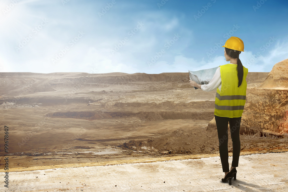 Asian business woman wear yellow helmet looking blueprint to build office building