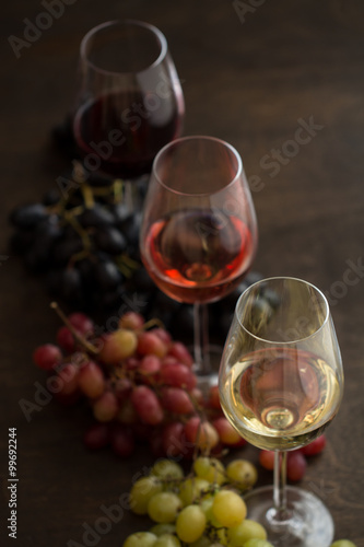 Three wineglasses of red, rose and white wine with three kinds of grapes on brown wood textured table