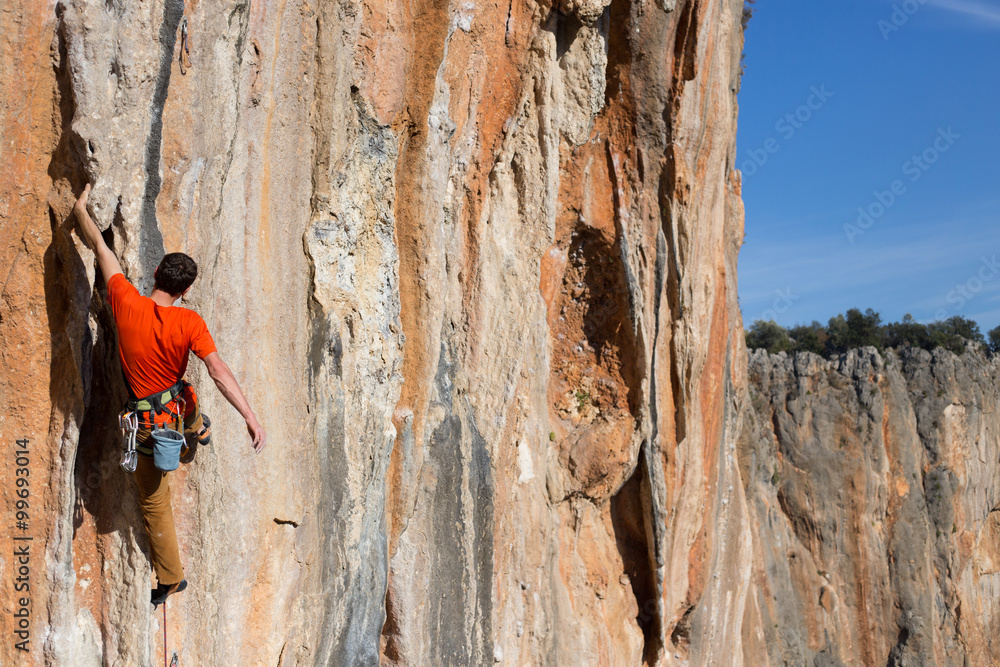 Young man climbs on a rocky wall in a valley with mountains at sunrise. Young man climbs on a rocky wall in a valley with mountains at sunrise.
