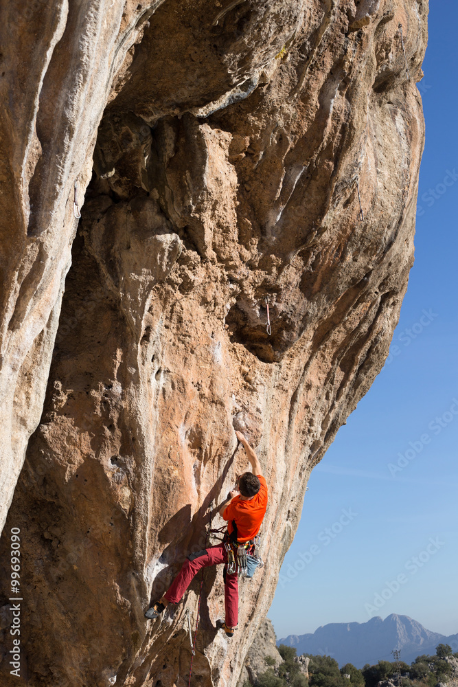 Fototapeta premium Young man climbs on a rocky wall in a valley with mountains at sunrise.