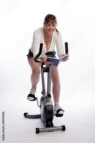 Woman working out on an exercise bike and reading a book