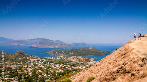 Two unrecognizable hikers enjoy the view over the Aeolian Islands from the volcano crater rim of Fossa di Vulcano