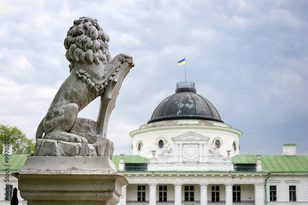 Obraz premium Statue of lion holding a shield in its paws. Regal lion leaning on empty heraldic shield near the castle entrance. The palace and park complex Manor Tarnowski, s.Kachanovka, Ukraine.