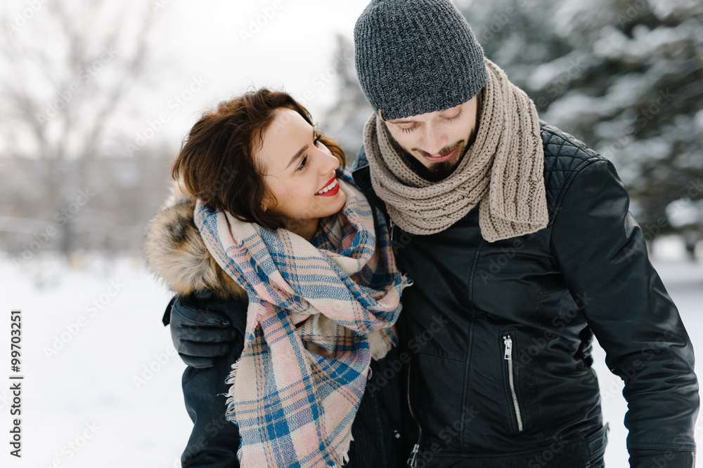 Cute young hipster couple having fun in winter park on a bright day hugging each other and smiling
Cute young hipster couple having fun in winter park on a bright day hugging each other and smiling
