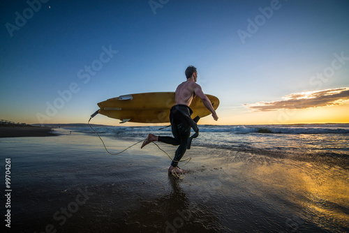 Photography Surfer running into water with surf board at sunset