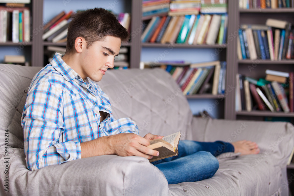 Handsome young man relaxing at home on a sofa in the living room reading a book or studying