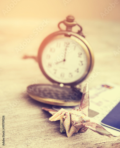 Fototapeta Naklejka Na Ścianę i Meble -  Financial time concept. Origami crane or bird made from a money note with watch time in out of focus background. Vintage style and filtered process.
