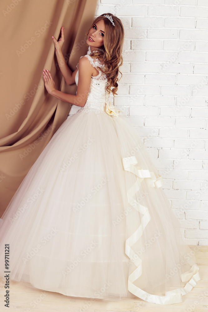 gorgeous young bride with blond curly hair, wears elegant wedding dress and crown