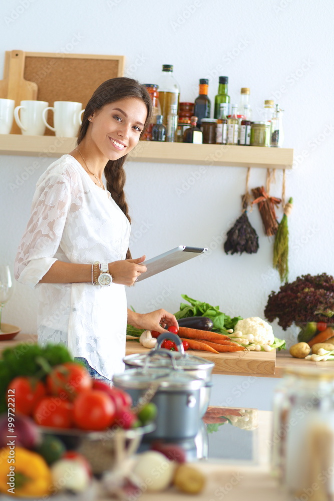Young woman using a tablet computer to cook in her kitchen Young woman using a tablet computer to cook in her kitchen