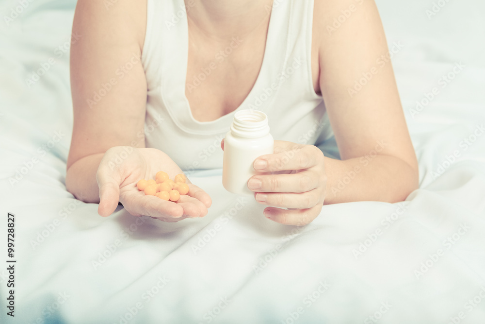 woman in her pajamas in bed holding yellow pills woman in her pajamas in bed holding yellow pills