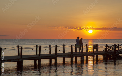 couple enjoying romantic walk on pier by ocean during sunset
