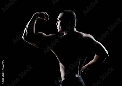 Wallpaper Mural bodybuilder demonstrates biceps back view on a dark background Torontodigital.ca