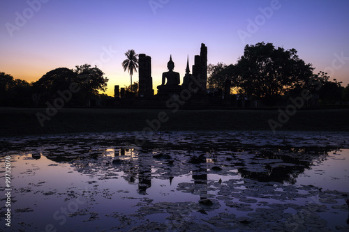 Reflection in a lotus pond of an ancient buddha statue at Sukhothai Historical Park, Mahathat Temple, Thailand. Sunset.