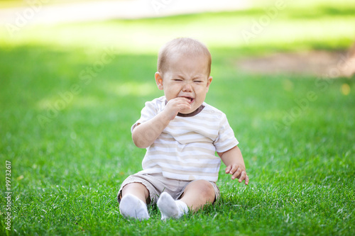 Little boy crying while sitting on grass in park © Andrey Bandurenko