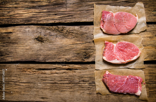 Steaks from raw fresh meat. On wooden background.