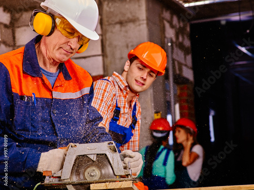 Group people builders working with circular saw. Brick wall in background.
