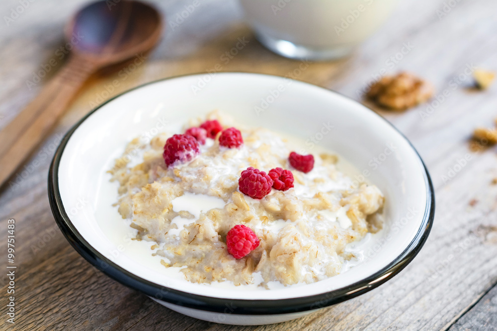Oatmeal porridge with raspberries and milk on textured wooden table Oatmeal porridge with raspberries and milk on textured wooden table