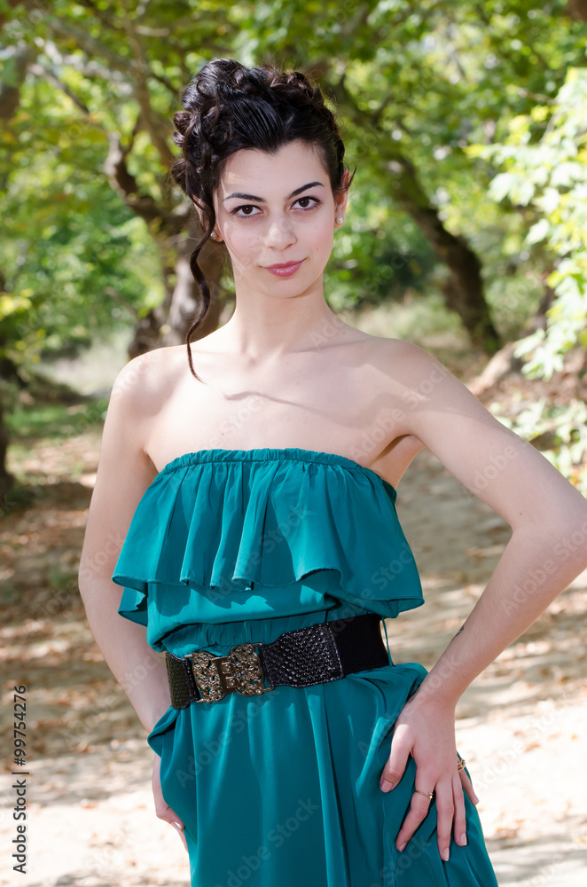 Fashion slim woman wearing green dress standing in the middle of a dirt road, leaves of trees on the ground. Gathered hair together style Fashion slim woman wearing green dress standing in the middle of a dirt road, leaves of trees on the ground. Gathered hair together style