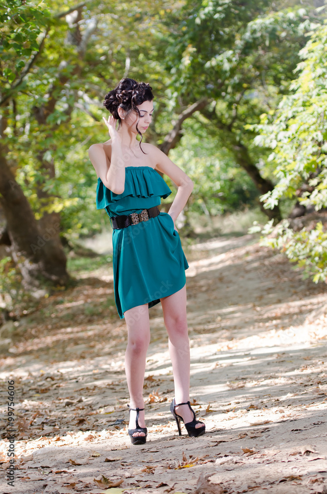 Fashion slim woman wearing green dress standing in the middle of a dirt road, leaves of trees on the ground. Gathered hair together style Fashion slim woman wearing green dress standing in the middle of a dirt road, leaves of trees on the ground. Gathered hair together style