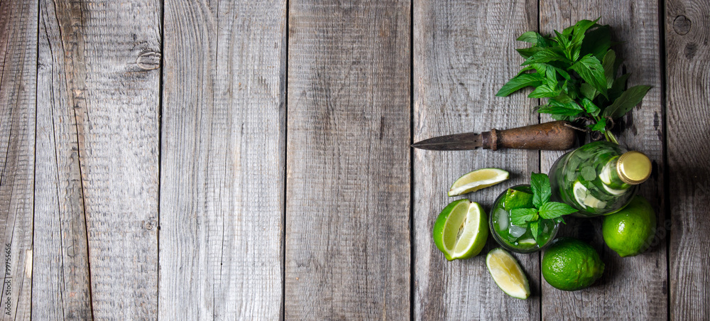 Cocktail in glass and bottle , also mint and limes on a wooden table . Free space for text. Cocktail in glass and bottle , also mint and limes on a wooden table . Free space for text.