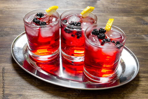 Berry cocktails in glass with ice and lemon on wooden table . photo