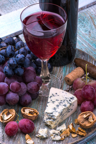 Red wine bottle, grapes, walnuts and cheese on a wooden background
