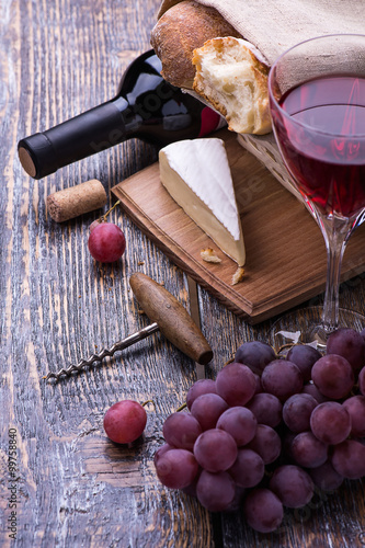 Red wine bottle, grapes, walnuts and cheese on a wooden background