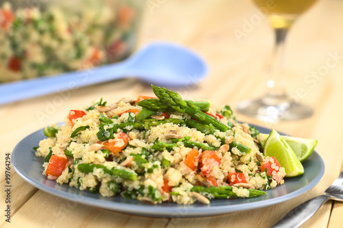 Vegetarian quinoa dish with green asparagus and red bell pepper, sprinkled with parsley and roasted sunflower seeds, lime wedges on the side (Selective Focus, Focus on the asparagus heads on the dish)