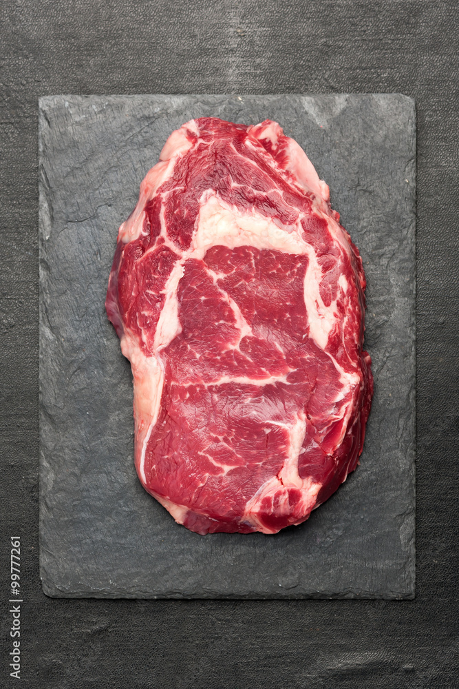 Raw ribeye steak on a slate board. Top view